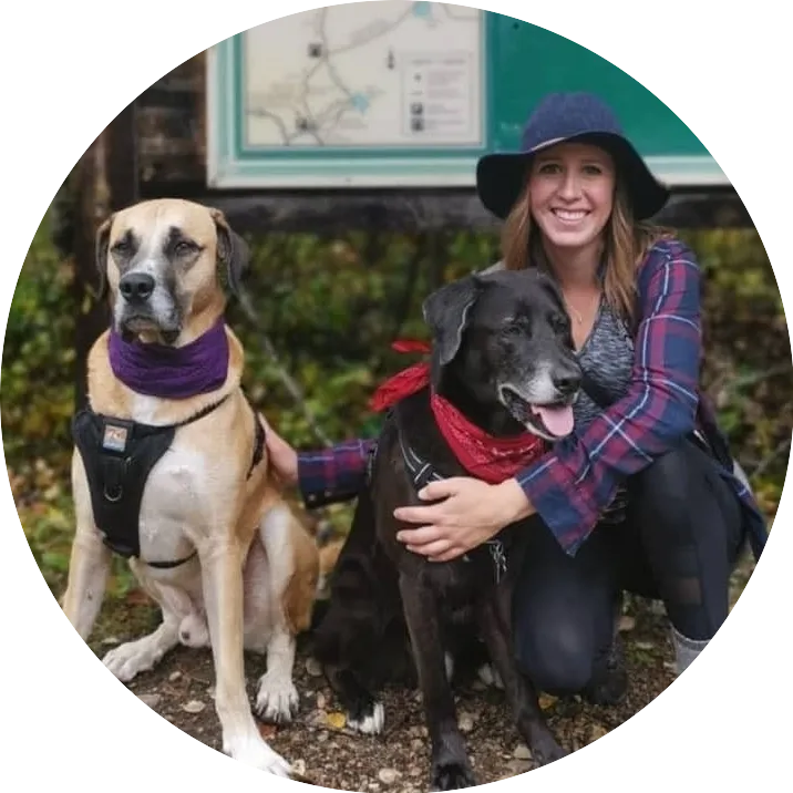 a woman with two dogs in front of a hiking trail